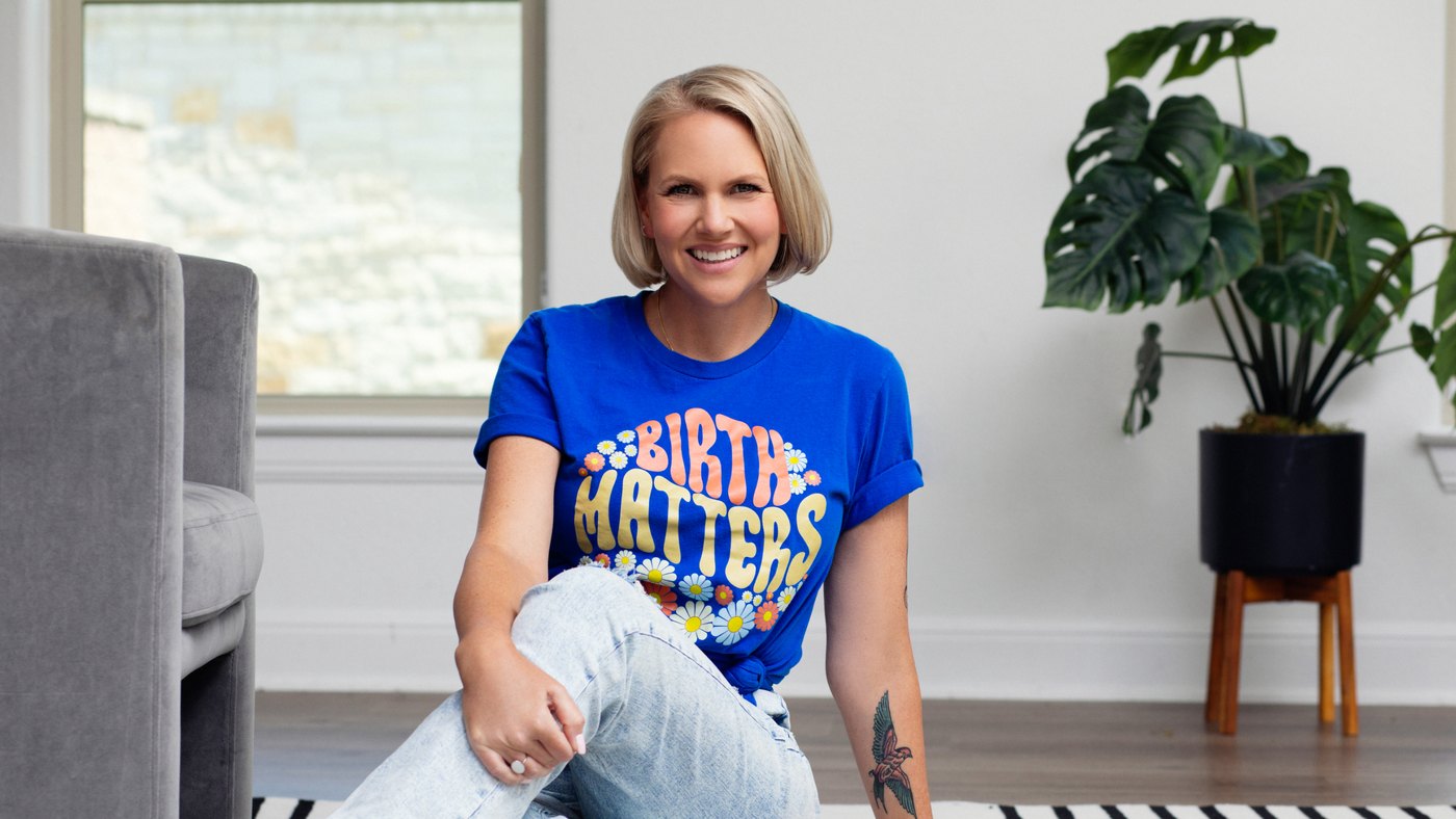 SarahBeth Bolin, LCSW, sitting on the floor of a sunlit room in a blue t-shirt printed “Birth Matters”.